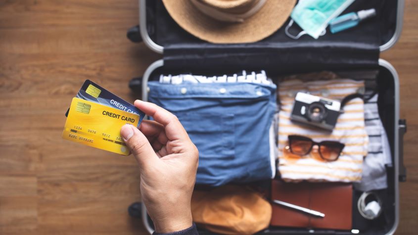 Person holding credit cards with suitcase in the background