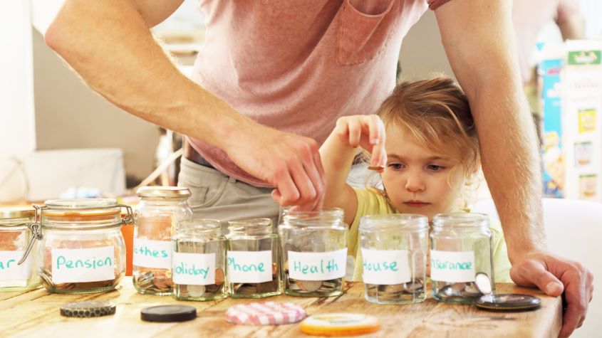 Young girl and father putting money into savings jars