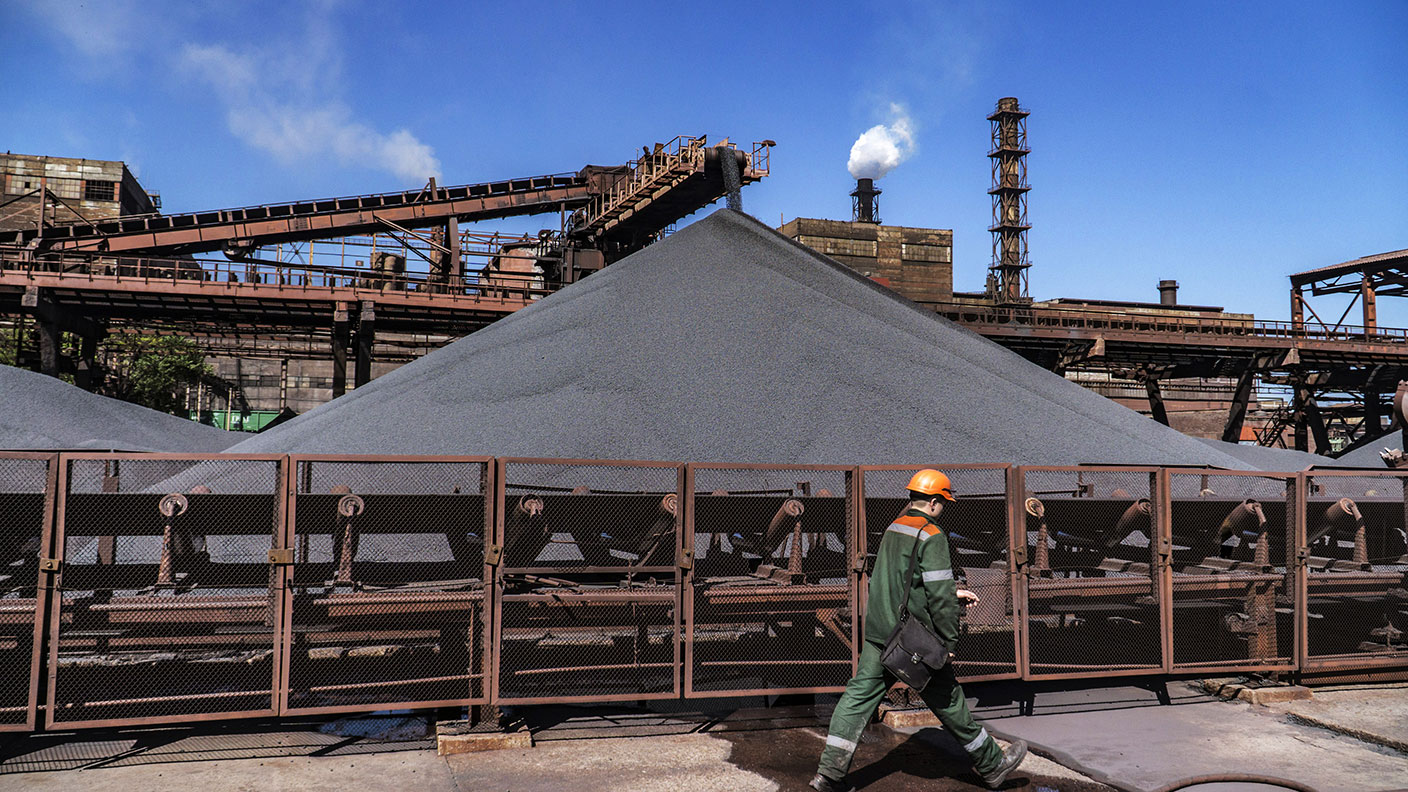 A worker walks past outdoor stores of iron ore pellets