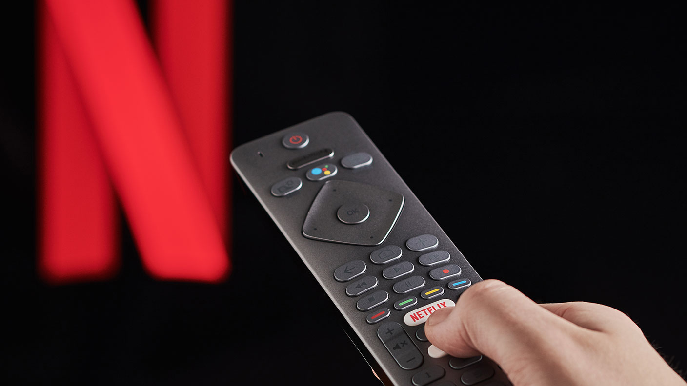 hand pressing the Netflix button on a TV remote control