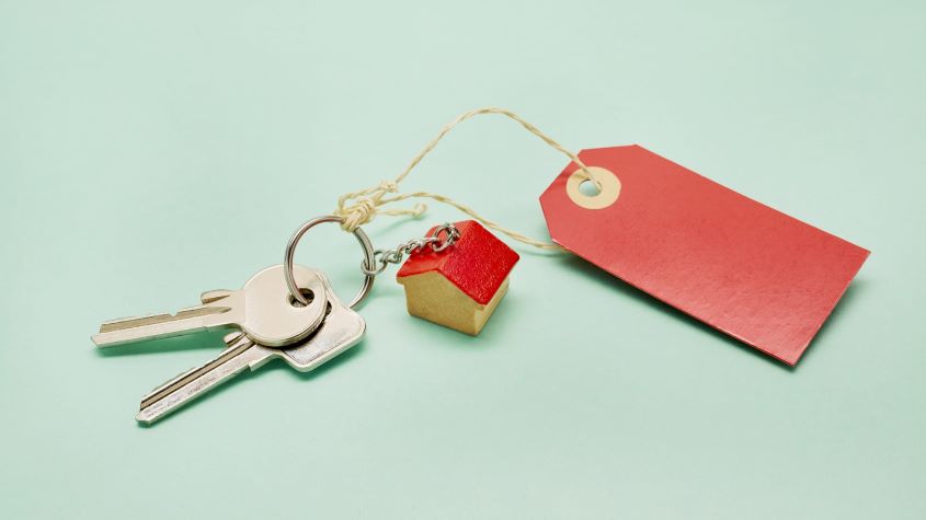 A keyring with keys, a small house and red price tag on turquoise background