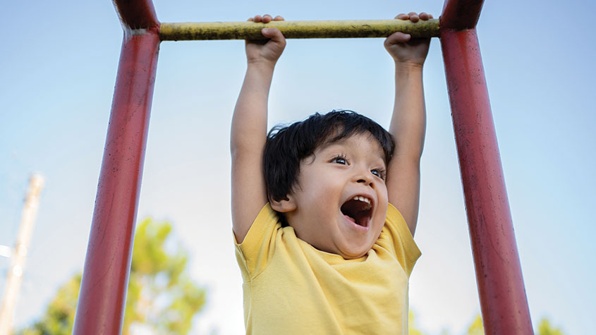 Boy swinging on playground bars