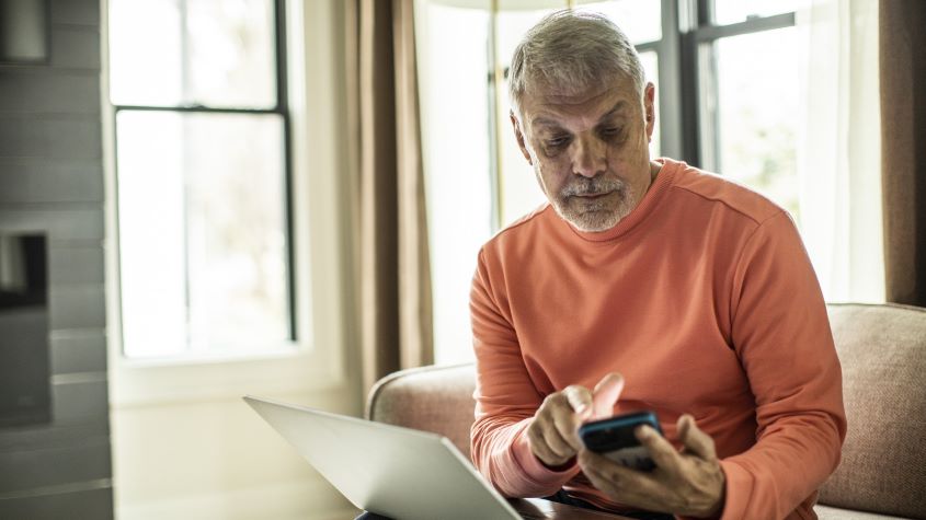 Senior man using laptop computer and smartphone at home