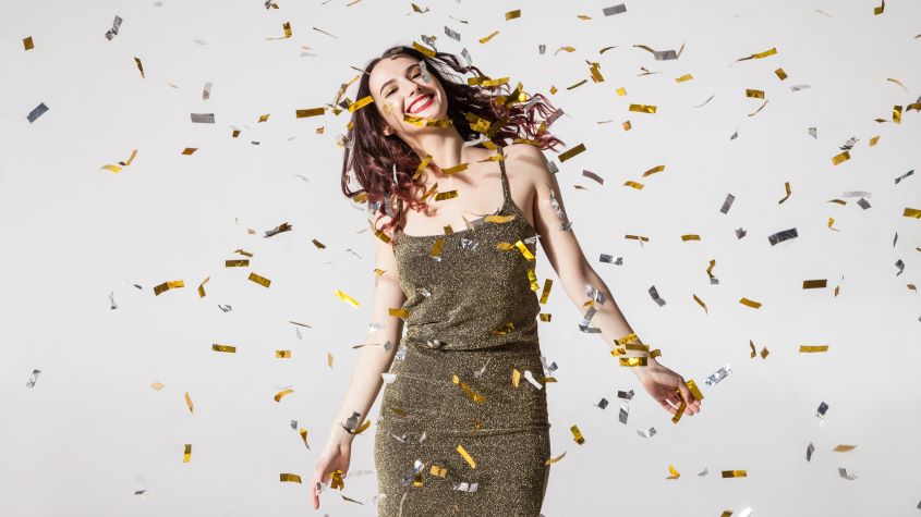 Woman smiling while dancing under falling confetti