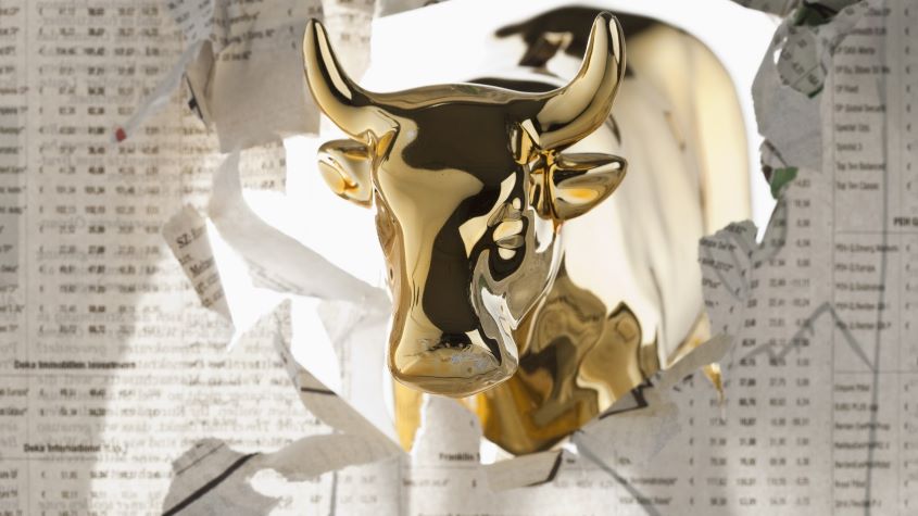 A golden bull breaking through the finance section of a newspaper